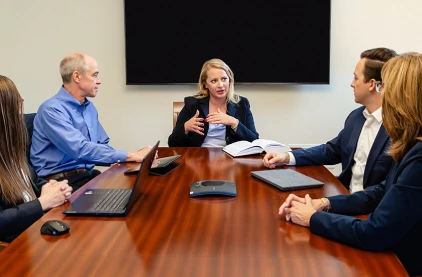 Female attorney making a point at the head of the conference table as colleagues listen.